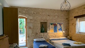 A room with a stone wall, two beds, a painting, a hanging light fixture, and a window. - Richiami di Sicilia (Modica)