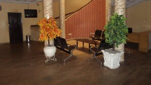 A lobby with a marble column, a staircase, a reception desk, and two chairs. - Golden Astoria Hotel (Abuja)