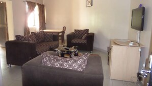 A living room with a sofa, two armchairs, a coffee table, a TV, and a small cabinet. - Golden Astoria Hotel (Abuja)