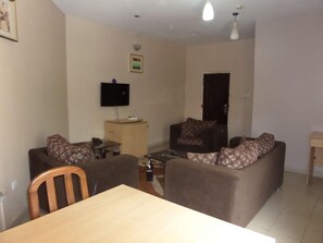 Un salon comprenant un canapé, une table en bois, un téléviseur fixé au mur et un meuble.