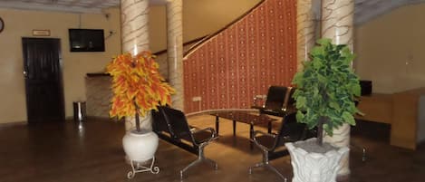 A lobby with a marble column, a staircase, a reception desk, and two chairs.