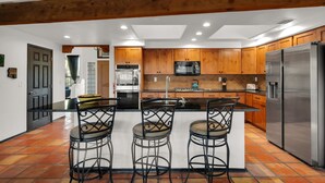 A modern kitchen with wooden cabinets, a stainless steel refrigerator, and a central island with bar stools. - Sonoran gem in Hidden Valley with POOL! (Tucson)