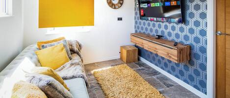A living room with a sofa, a television mounted on the wall, a wooden sideboard, and a patterned wall.