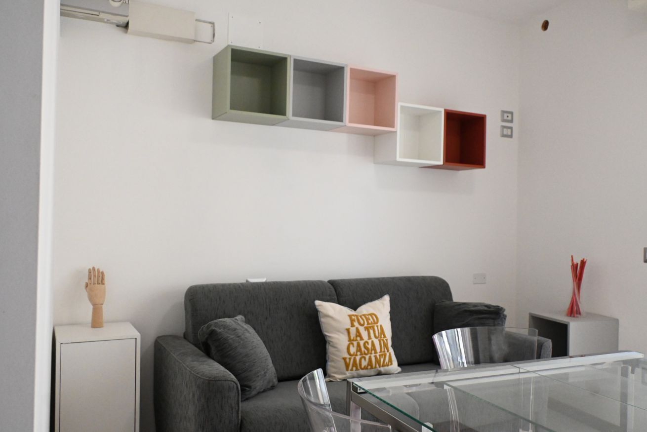 Una sala de estar moderna con un sofá gris, una mesa de centro de vidrio y un mueble de pared con estantes vacíos.