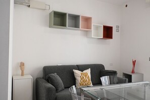 A modern living room with a grey sofa, a glass coffee table, and a wall-mounted shelf unit with empty compartments. - SE170 – Senigallia, seafront studio with air conditioning (Senigallia)