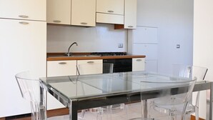 A modern kitchen with white cabinets, a glass dining table, and clear chairs. - SE170 – Senigallia, seafront studio with air conditioning (Senigallia)