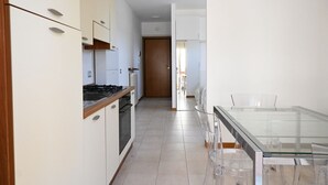 A modern kitchen with white cabinets, a glass dining table, and a view into the adjacent room. - SE170 – Senigallia, seafront studio with air conditioning (Senigallia)