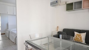 A modern room with a glass dining table, a grey sofa with a cushion, a small white side table, and a bed with white bedding. - SE170 – Senigallia, seafront studio with air conditioning (Senigallia)