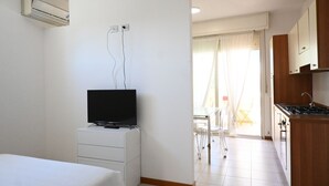 A room with a bed, a TV on a stand, a kitchenette, and a sliding glass door leading to a balcony. - SE170 – Senigallia, seafront studio with air conditioning (Senigallia)