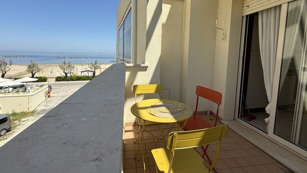 A balcony with a table and chairs, a view of the beach, and a building with a sliding door. - SE170 – Senigallia, seafront studio with air conditioning (Senigallia)