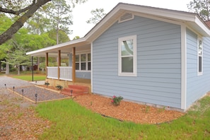A light blue single-story house with a covered porch, a small front yard with mulch and plants, and a driveway.