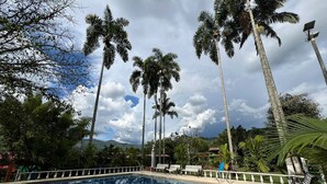 Una piscina circondata da palme e panchine, con cielo sereno e montagne sullo sfondo.