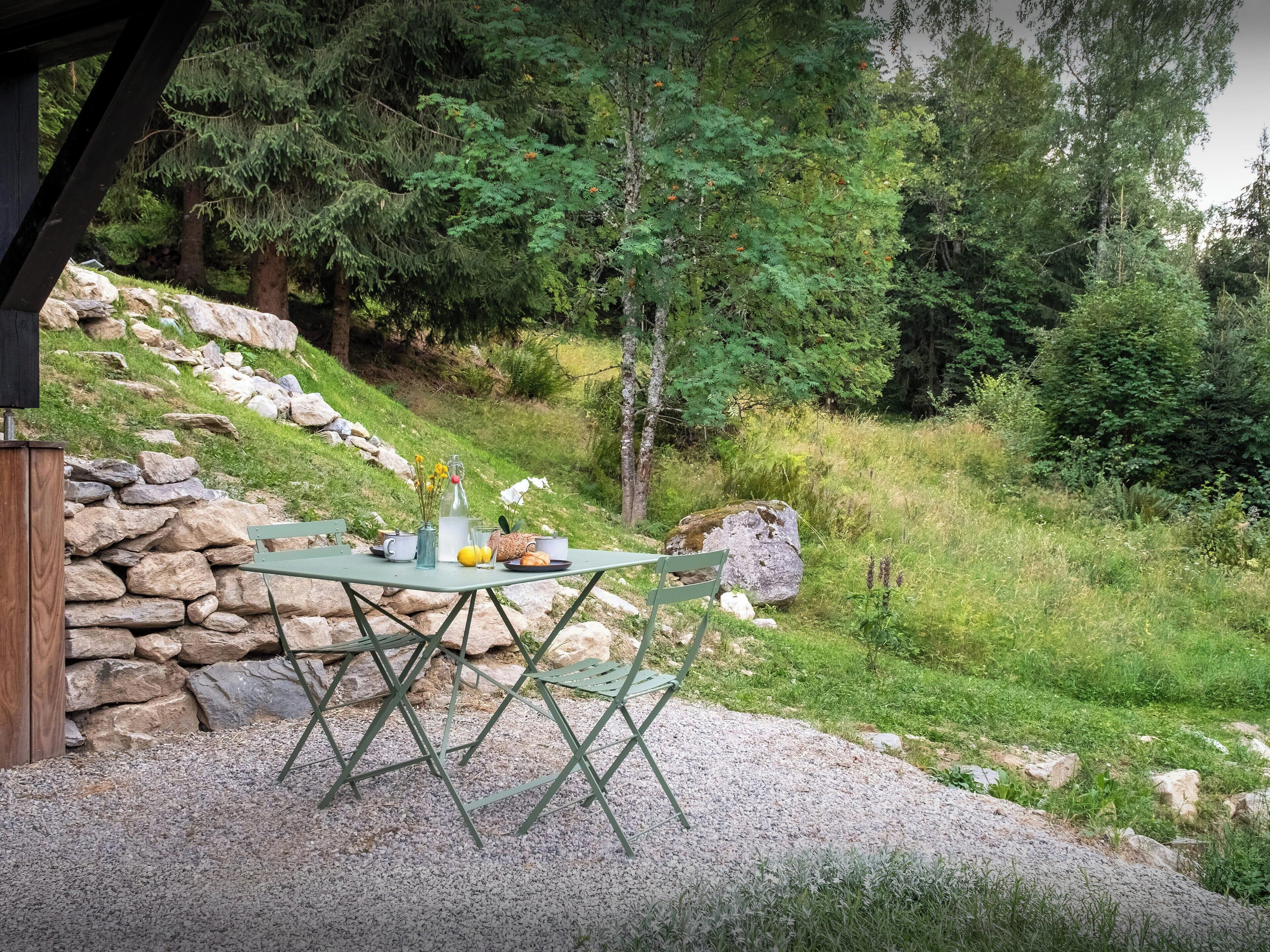 Un área de comedor al aire libre con una mesa y sillas, rodeada por un muro de piedra y follaje.