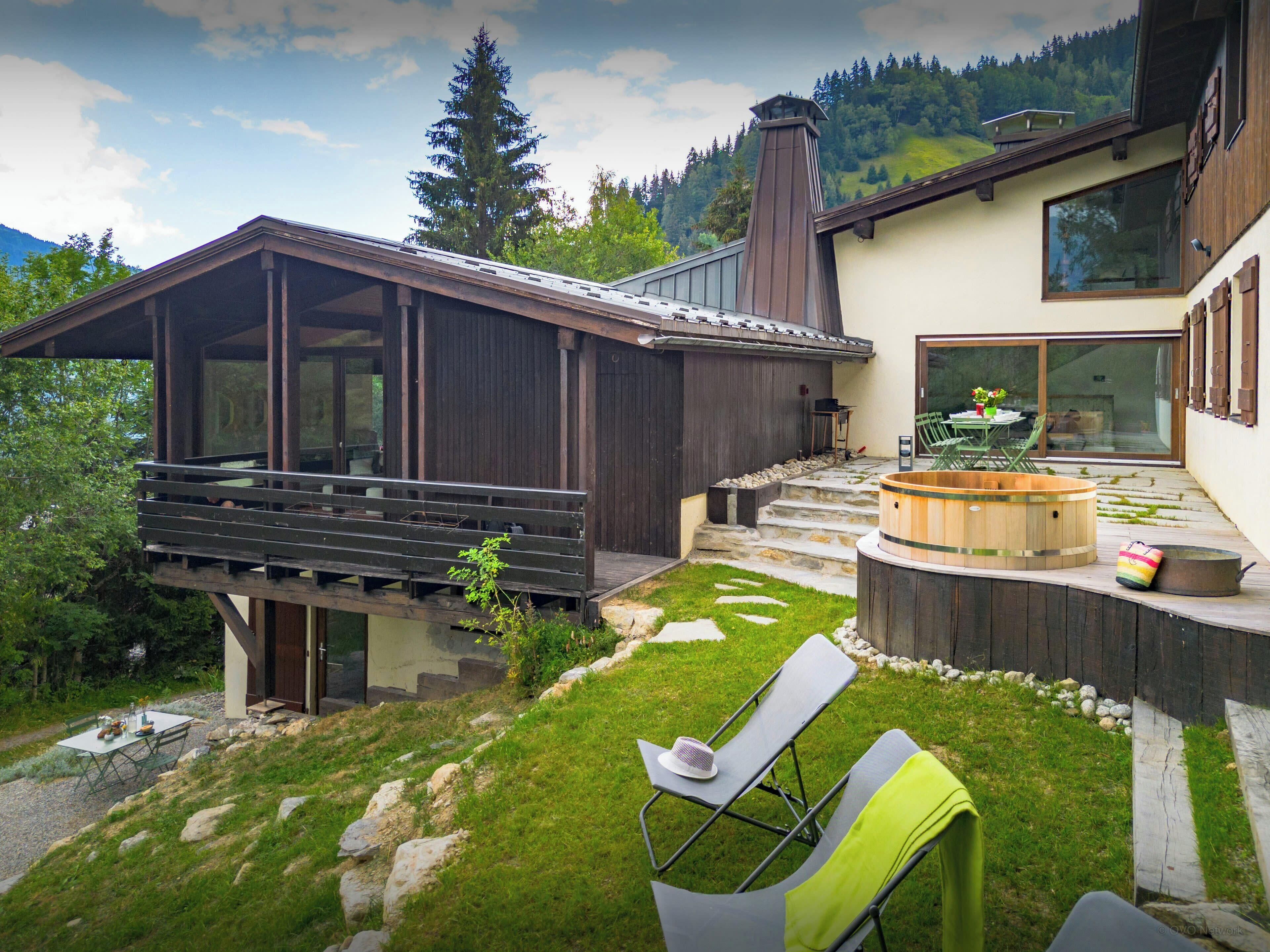 A modern house with a wooden deck, a hot tub, and a dining area.