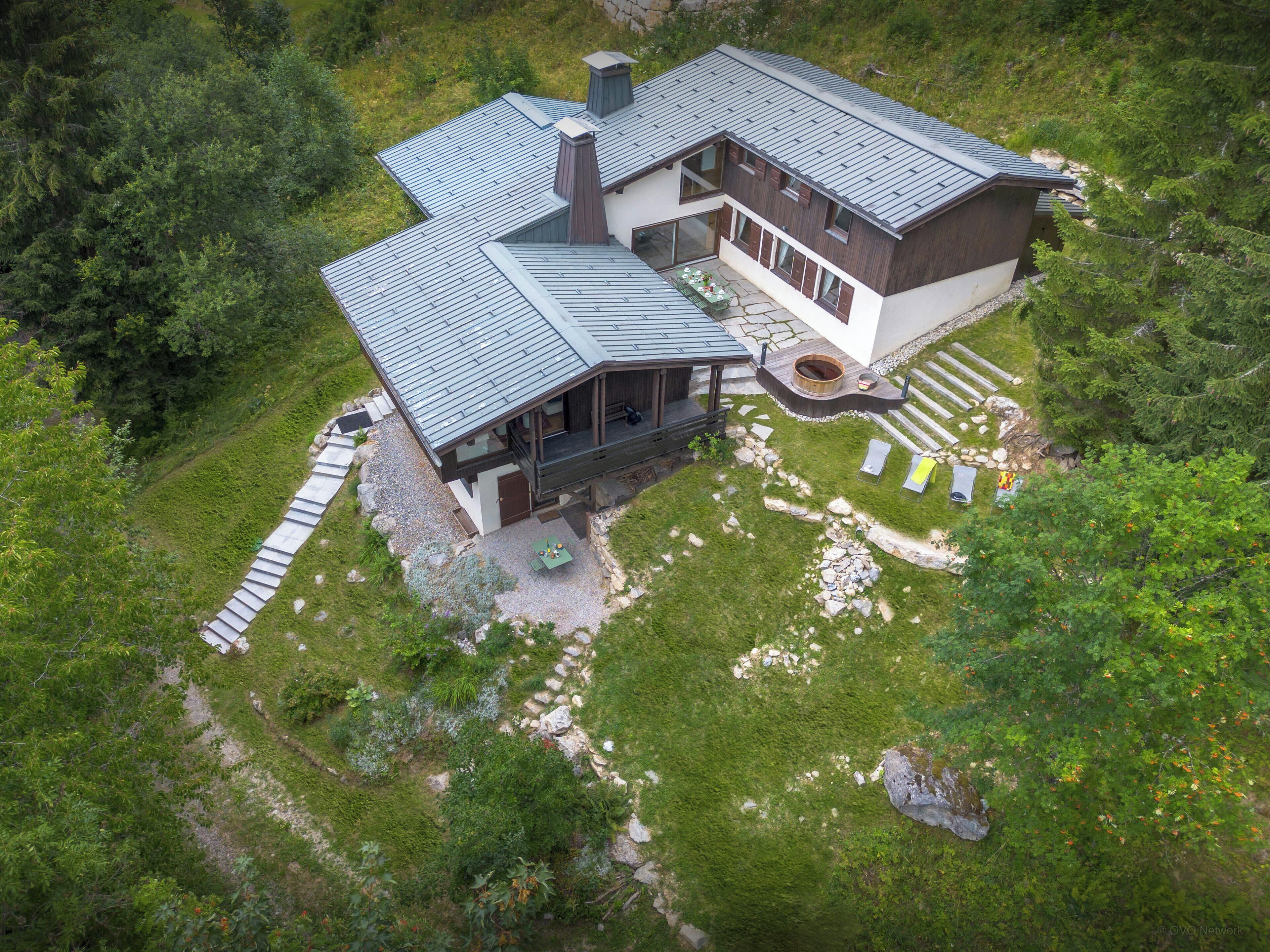 A modern two-story house with a sloped roof, a covered outdoor seating area, and a stone pathway leading to the entrance.