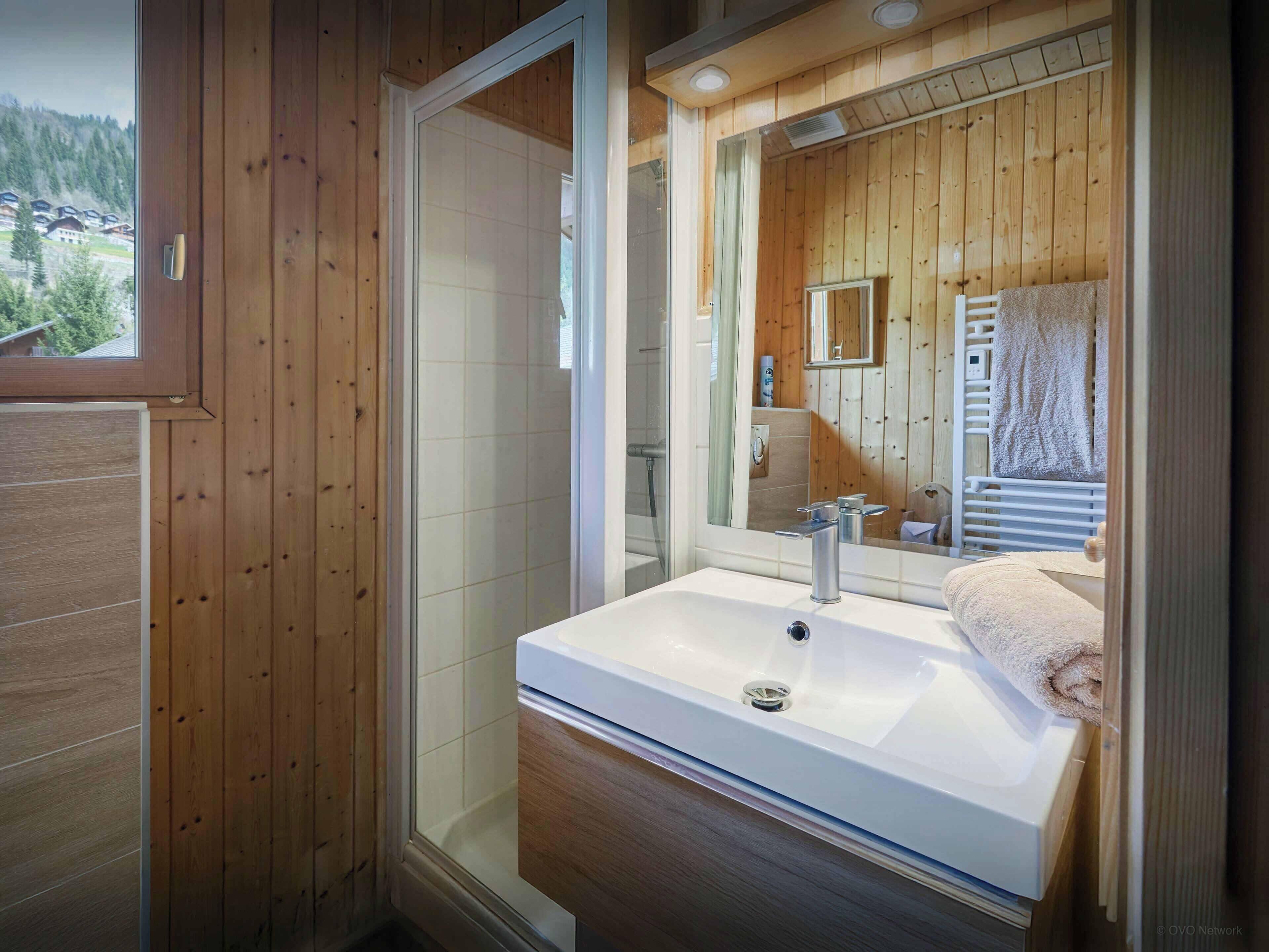 Une salle de bain moderne avec un grand miroir, un lavabo blanc et un espace douche.