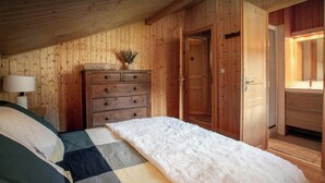 A bedroom with a bed, wooden wardrobe, and a bathroom with a mirror. - Chalet Rochamour - mountain holiday for 14 with spa - OVO Network (Châtel)