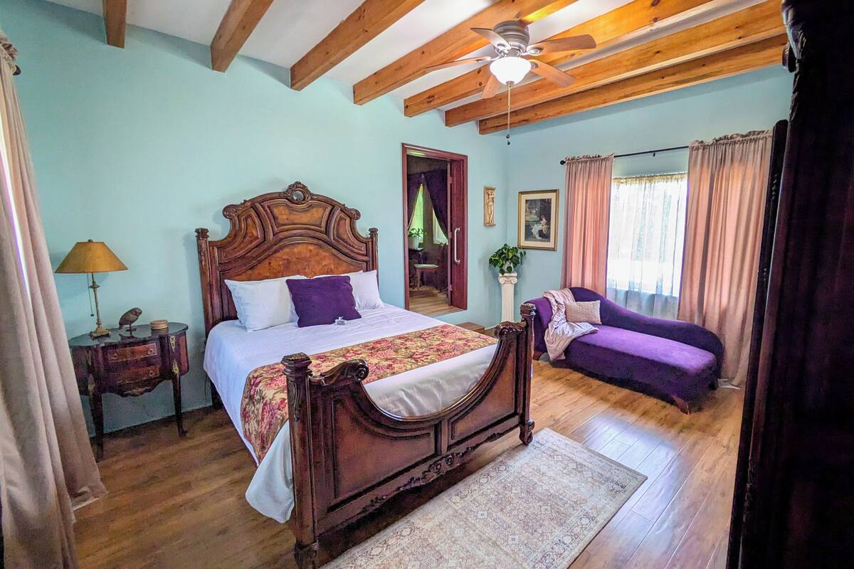 A bedroom with a wooden bed, a ceiling fan, a sofa, and a window with curtains.