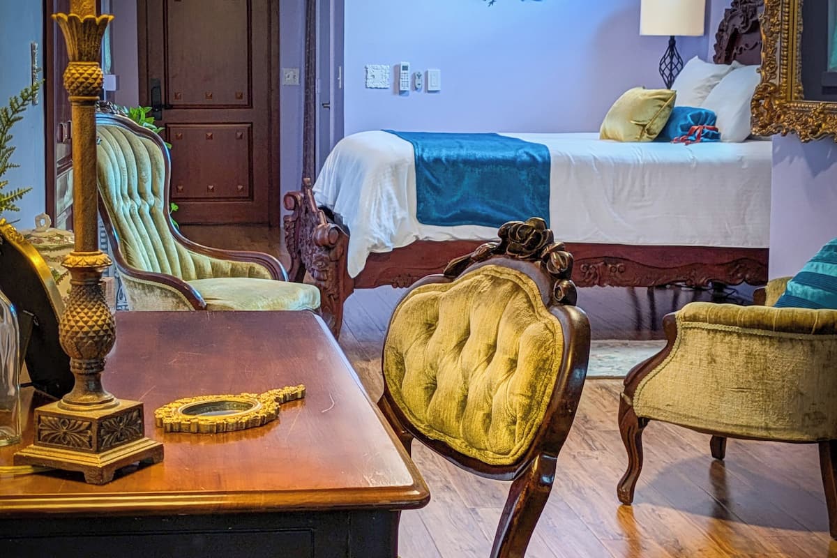 A traditional room with a wooden floor, a bed with a blue and white bedspread, a wooden chair, a table with a lamp, and a decorative wall piece.