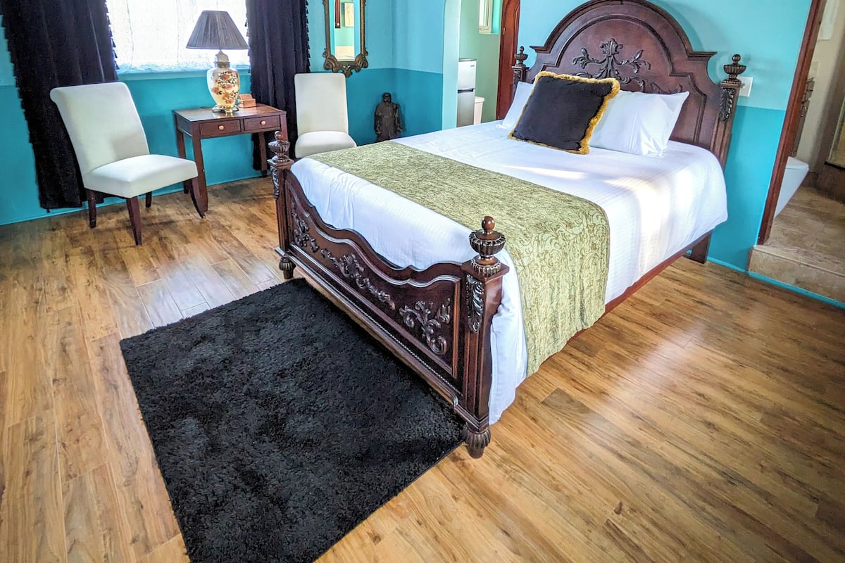 A bedroom with a wooden bed, a ceiling fan, a black rug, and a window with curtains.