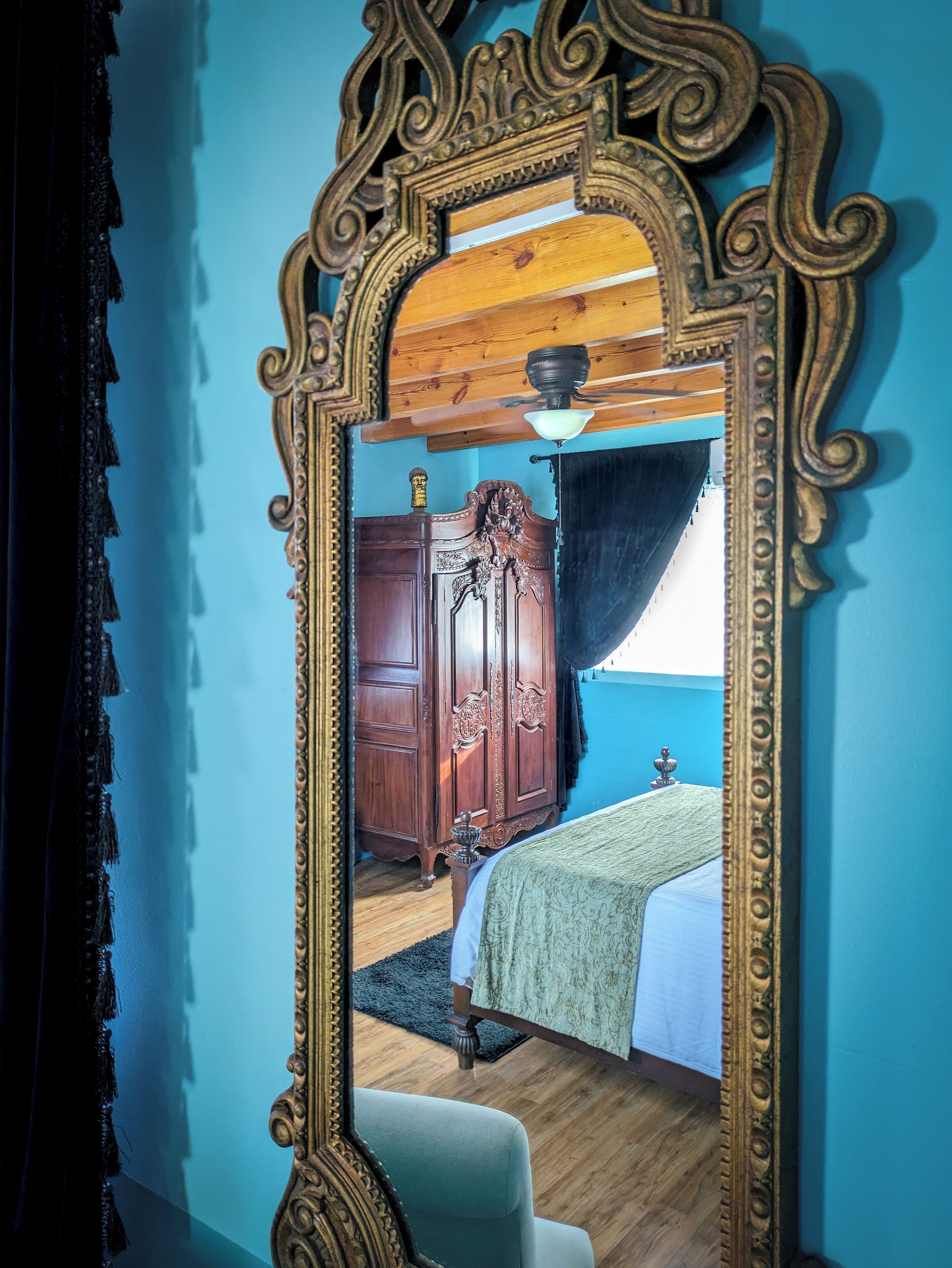 Un dormitorio con un espejo grande y ornamentado, un armario de madera y una cama con cubrecama verde.