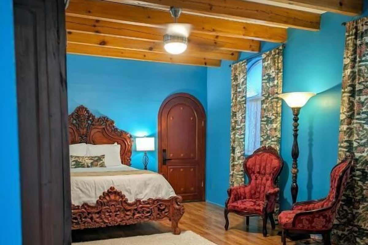 A bedroom with a wooden bed, two red upholstered chairs, a wooden wardrobe, and a blue wall.