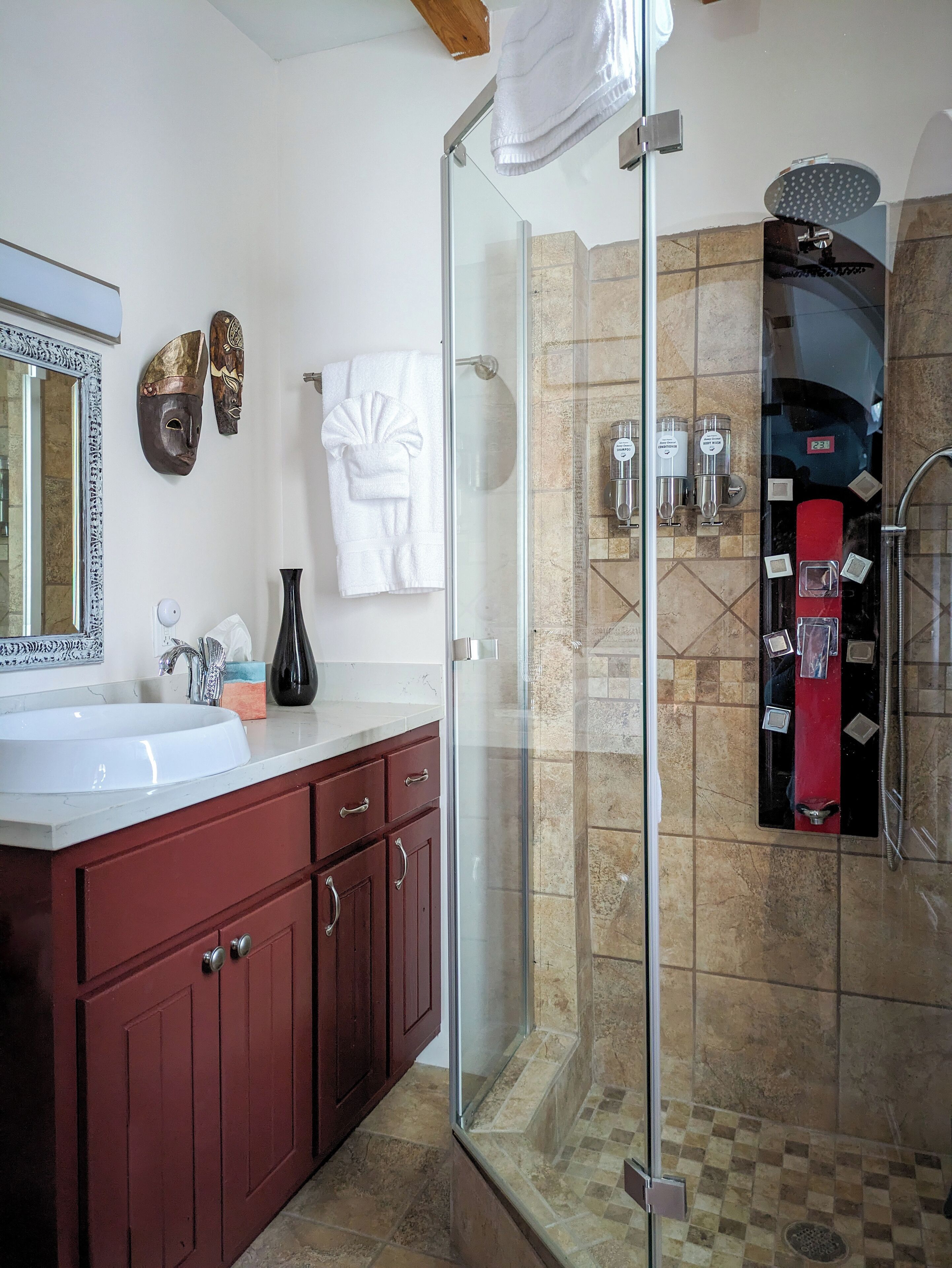 A modern bathroom with a glass-enclosed shower, a vanity with a white sink, and decorative masks on the wall.
