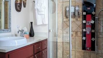 A modern bathroom with a glass-enclosed shower, a vanity with a white sink, and decorative masks on the wall.