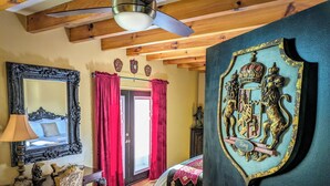 Une pièce avec un plafond en bois, un grand miroir, des rideaux rouges, un lit recouvert d’une courtepointe rouge et or, et un blason accroché au mur.