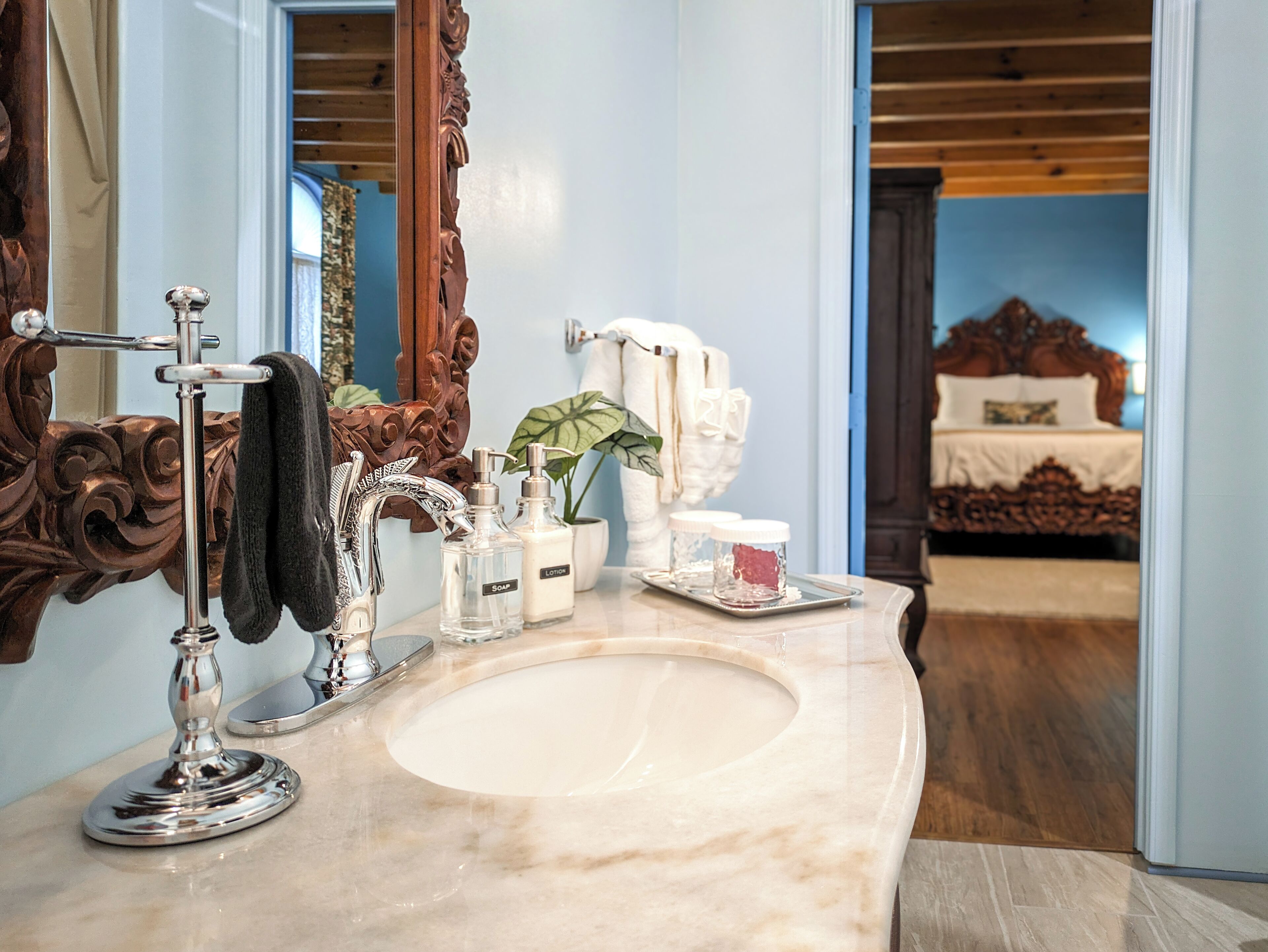 Un baño con lavamanos de mármol, un espejo grande y decorativo, y artículos de tocador sobre la encimera.