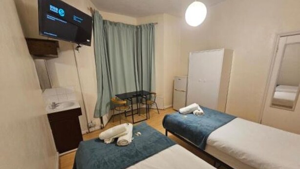 A hotel room with two beds, a desk, a chair, a TV, and a whiteboard. - Bruce Rooms – Your Comfortable Retreat in Tottenham (London)