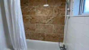 A bathroom with a bathtub, a shower curtain, and tiled walls. - Bruce Rooms – Your Comfortable Retreat in Tottenham (London)