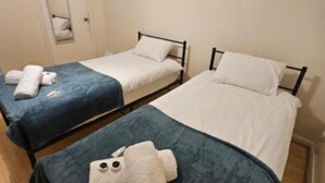 A hotel room with two single beds, each with a blue bedspread and white pillows. There is a white stuffed toy on the floor between the beds. - Bruce Rooms – Your Comfortable Retreat in Tottenham (London)