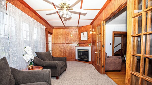 A room with wooden paneling, a fireplace, two armchairs, a side table with a vase, and a door leading to another room. - Spacious 5 BDR, 2.5 BATH - Updated & Prime! Lots of Parking! Sleeps up to 16! (Cedar Rapids)