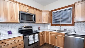 A kitchen with wooden cabinets, a stainless steel oven, a dishwasher, and a window with blinds. - Spacious 5 BDR, 2.5 BATH - Updated & Prime! Lots of Parking! Sleeps up to 16! (Cedar Rapids)