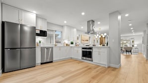 Une cuisine moderne dotée d’appareils électroménagers en acier inoxydable, de meubles blancs et d’un plancher en bois.