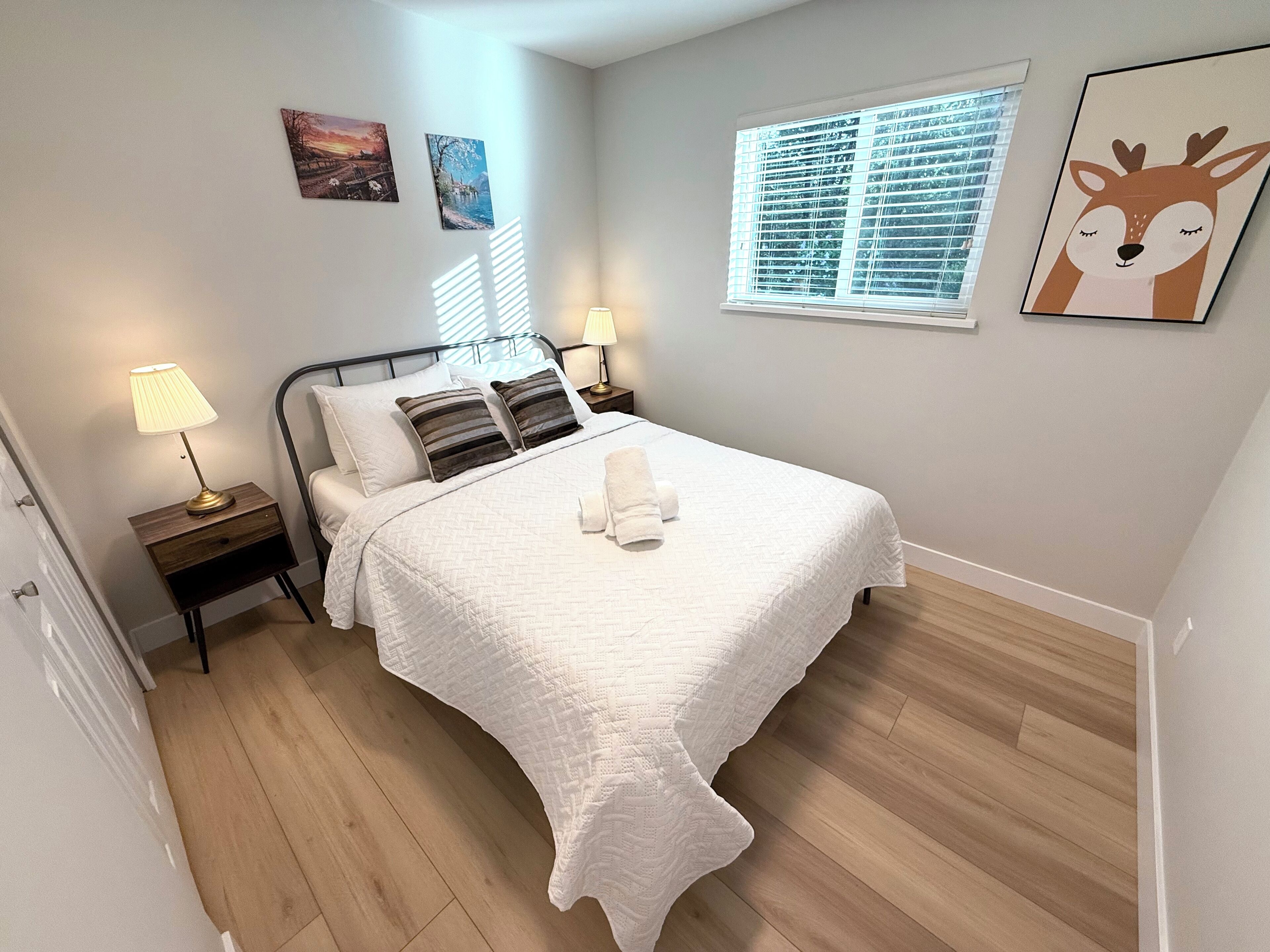Una camera da letto ordinata con un letto, lampade da comodino, una finestra con persiane e decorazioni alle pareti.