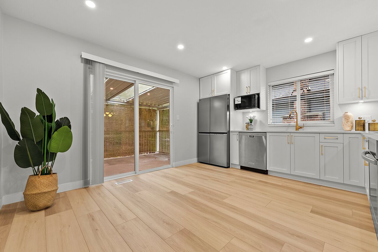 A modern kitchen with white cabinets, a stainless steel refrigerator, and a sliding glass door leading to a balcony.