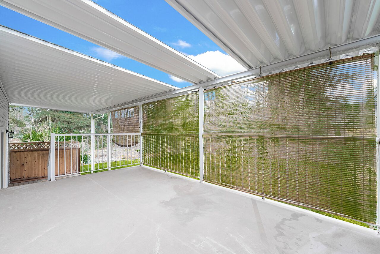 A covered patio area with a view of the surrounding landscape, a wooden fence, and a concrete floor.