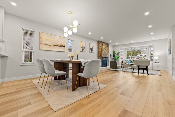 A spacious living room with a wooden floor, a dining area with a table and chairs, and a fireplace. - Vancouver Lake City Way Guesthouse (Burnaby)