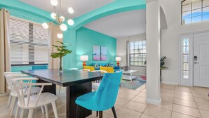 Une cuisine moderne avec un mur d’accent de couleur turquoise, des chaises blanches et un îlot central.