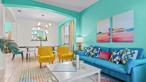 Un salon avec un mur de couleur turquoise, un canapé bleu, des fauteuils jaunes et une table basse blanche.