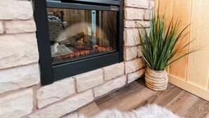 Una chimenea de piedra con puerta de vidrio, piso de madera y una planta en maceta a su lado.