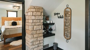 Un dormitorio con una pared de acento de piedra, una cama con cabecera de madera, una mesita de noche y una repisa con objetos decorativos.