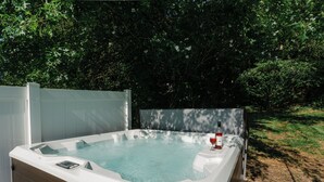 Un jacuzzi con cubierta de madera y recinto de vidrio, rodeado de exuberante vegetación.