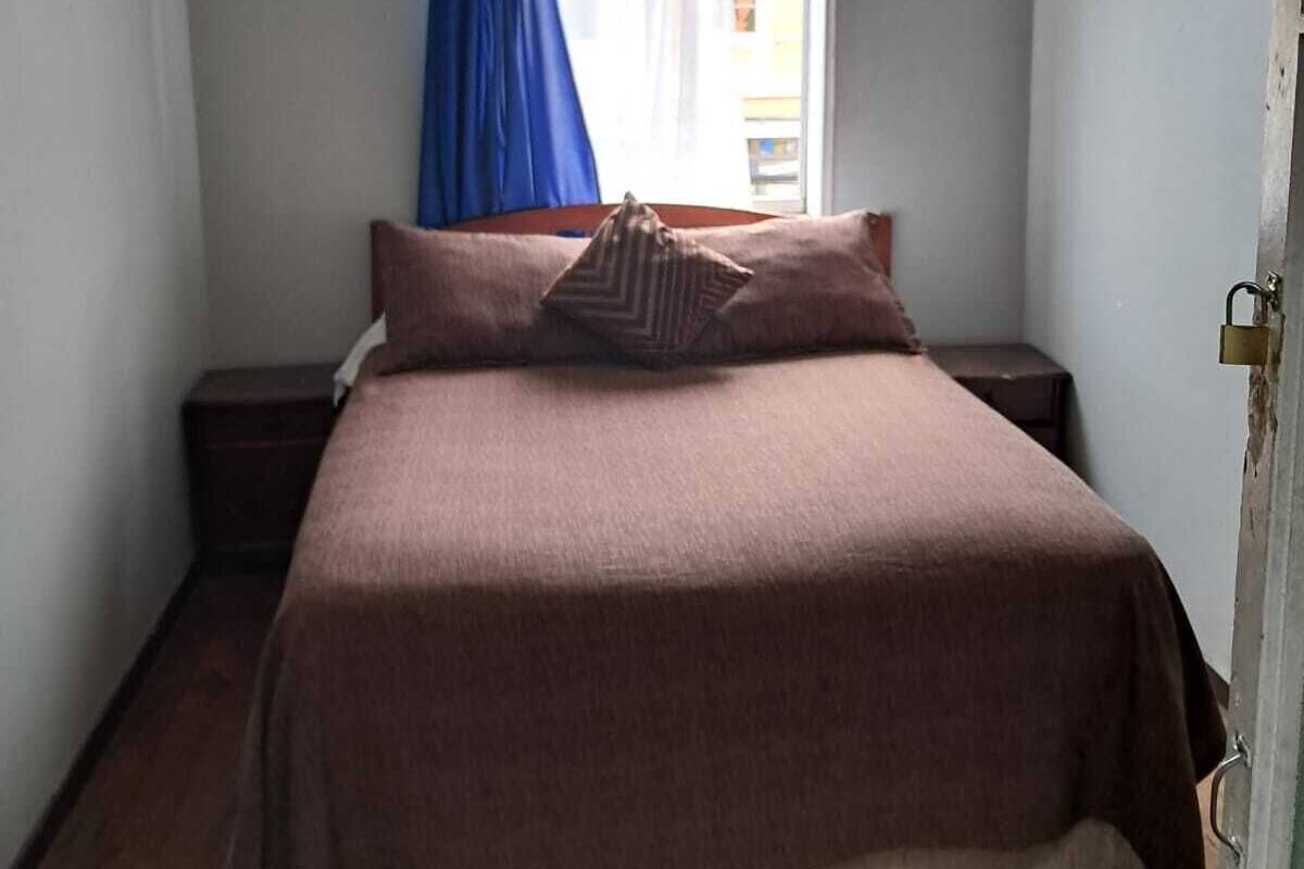 Una camera da letto con un letto, un comodino, una finestra con tende blu e una lampada a sospensione.