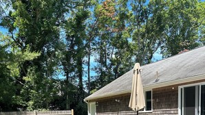 A backyard with a wooden deck, a barbecue grill, and a dining table with chairs. - Charming 3-bedroom house in West Hyannisport (Barnstable)