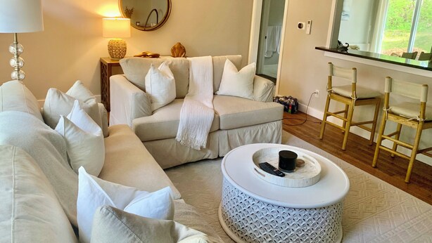A living room with a beige sofa, a round coffee table, and a wooden bar stool. - Charming 3-bedroom house in West Hyannisport (Barnstable)