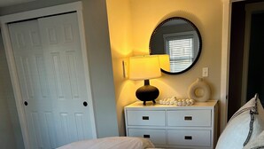 A neatly made bed with a textured white bedspread, a bedside table with a lamp, and a mirror above it. - Charming 3-bedroom house in West Hyannisport (Barnstable)