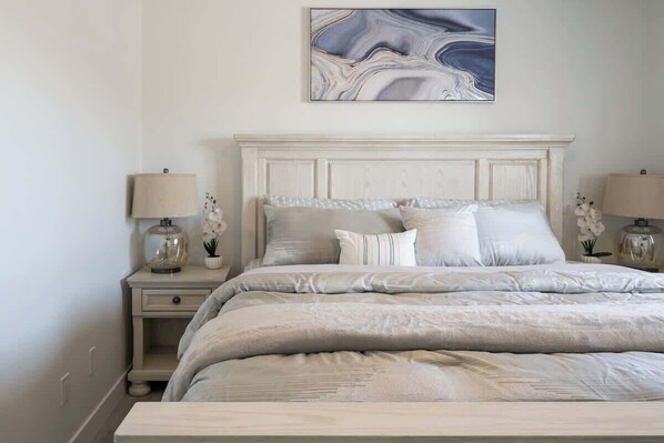 A bedroom with a large bed, two bedside tables with lamps, a marble artwork above the bed, and a white headboard.